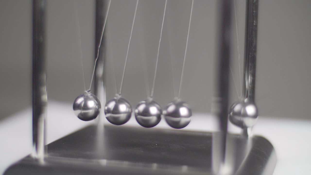 Slow motion: Newton's cradles swinging on a white minimal surface with a dark background in Slow Motion. Camera panning movement. Shot in 4K.