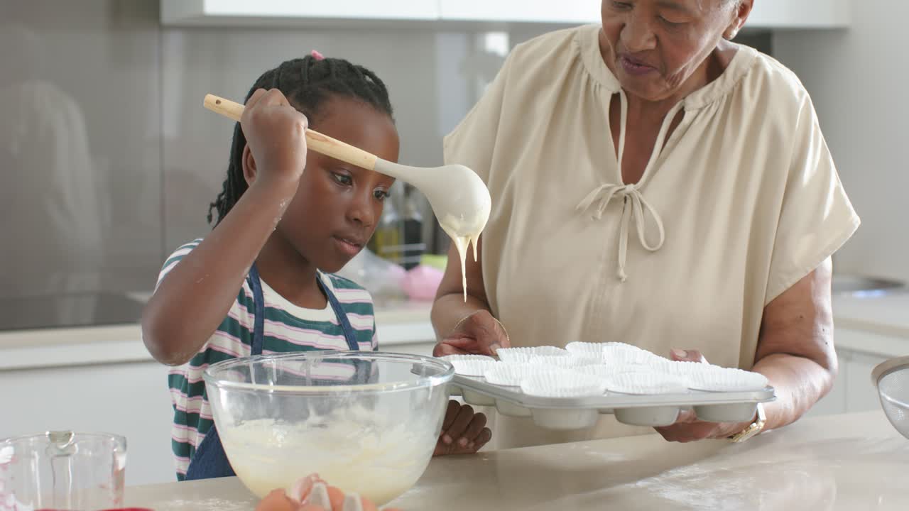 African American grandmother and granddaughter scooping batter pouring into tray on counter to bake