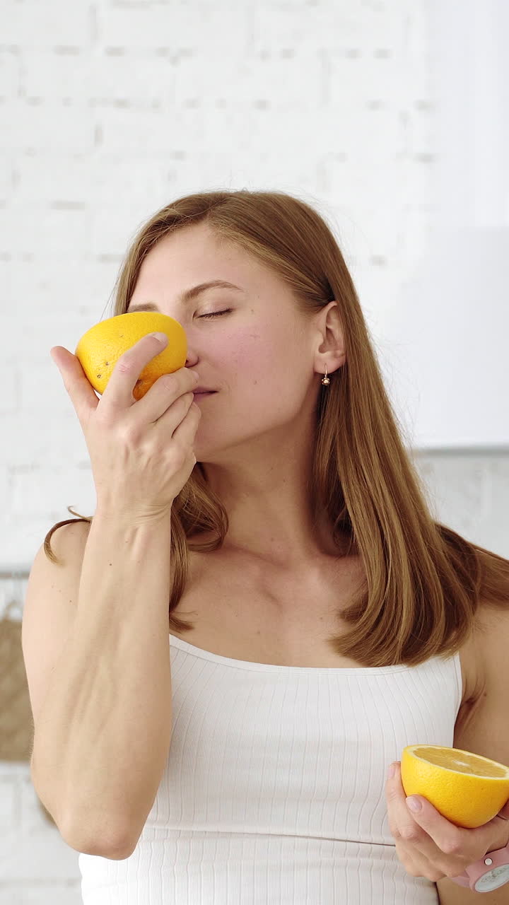 A cheerful girl covers her eyes with orange slices. Emotions in the white kitchen. Healthy eating. Vertical video