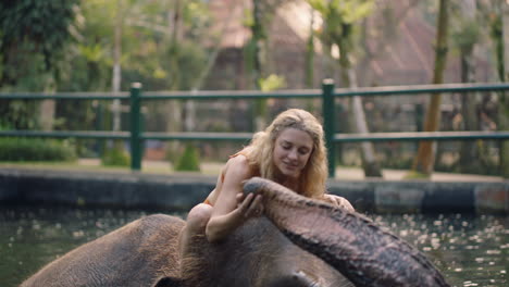 Reisefrau,-Die-Im-Zoo-Auf-Einem-Elefanten-Reitet,-Im-Pool-Spielt-Und-Wasser-Sprüht.-Touristin,-Die-Spaß-An-Einem-Exotischen-Urlaub-Im-Tropischen-Waldschutzgebiet-Hat