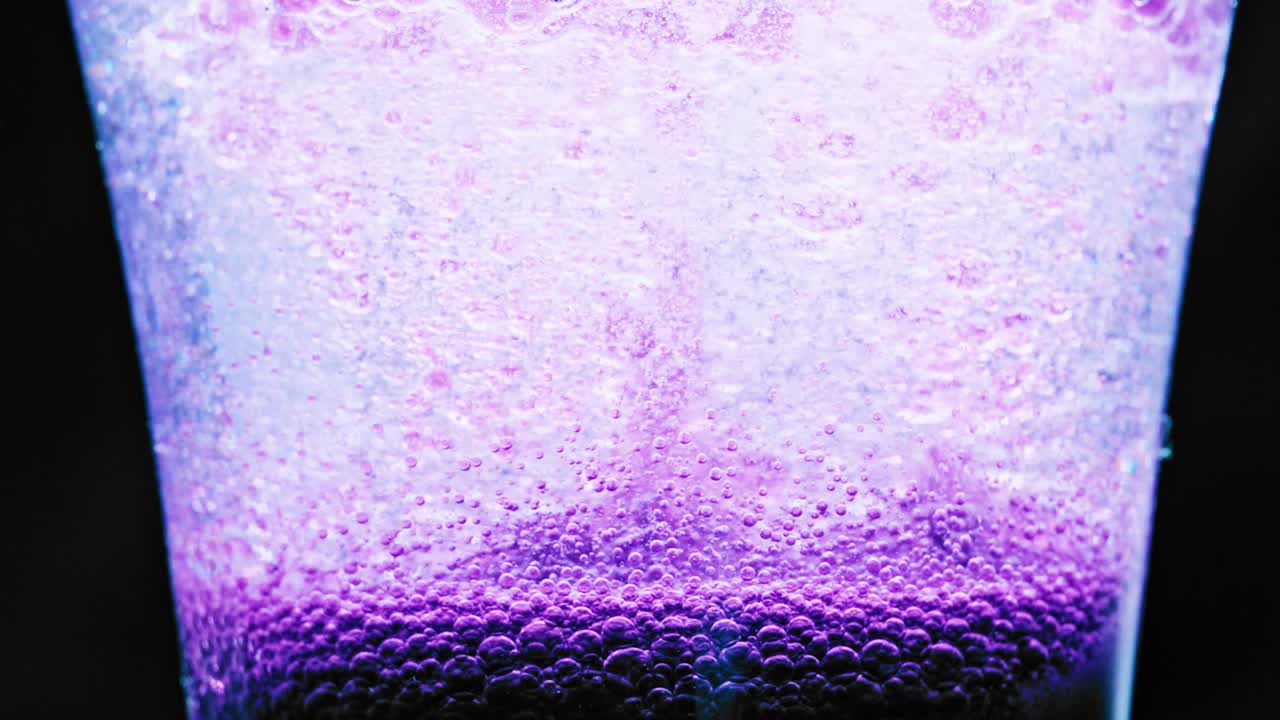 foto macro de burbujas violetas brillantes que se mueven hacia arriba en un vaso con fondo brillante
