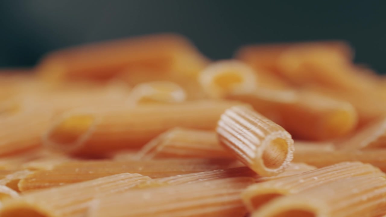 Pasta integrale biologica, maccheroni di semola di grano duro, penne rigate crude in una ciotola di legno. Filmato 4k di alta qualità