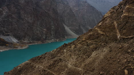 drone shot revealing attabad lake behind rocky mountain side, himalaya