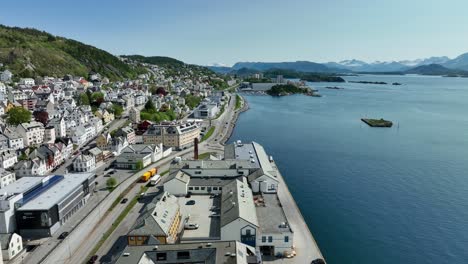 Cars-leaving-Aalesund-Norway-on-a-beautiful-summer-day---Aerial-facing-East-beside-road-E136-and-Color-Line-stadium-with-TINE-dairy-industry-building-below-drone