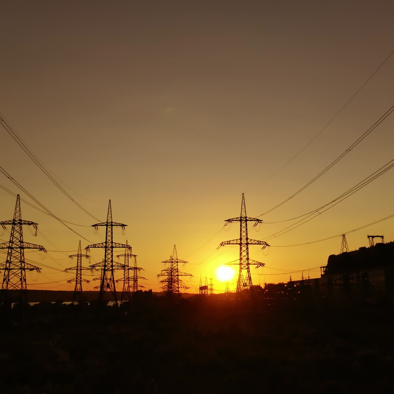 Electric power station in the evening. High voltage electric lines against the setting sun. Transmission lines. Motion camera back.