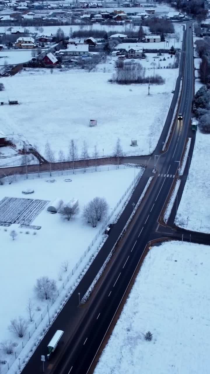 Aerial shot of a snow-covered road with a serene winter neighborhood surrounding it.