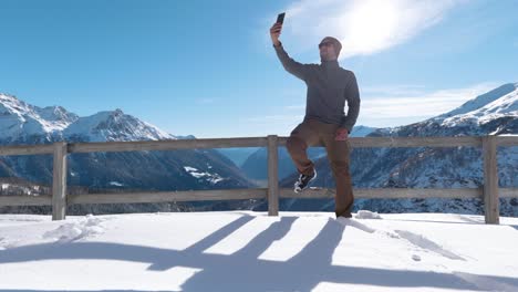 Young-caucasian-man-with-a-beanie-and-sunglasses-takes-a-selfie-with-his-smartphone-while-enjoing-the-view-on-a-sunny-day-in-the-mountains