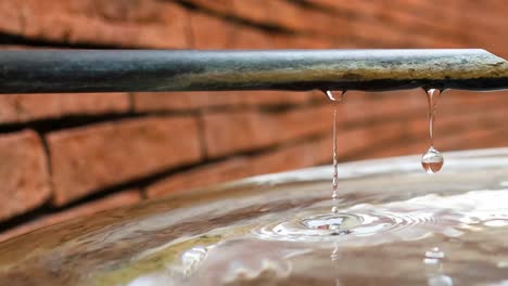 una gota de agua desciende de un grifo