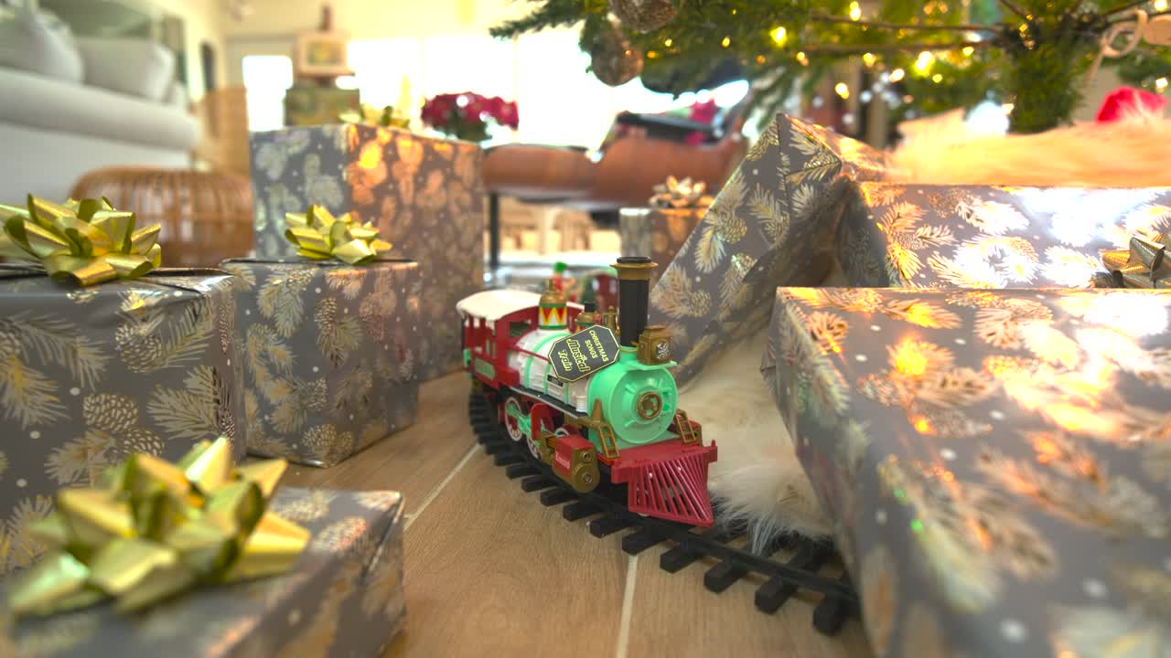 "Captivating stock footage: Glide beneath a festive Christmas tree, presents galore, showcasing a model train, spreading joy in a delightful reverse wide sliding shot