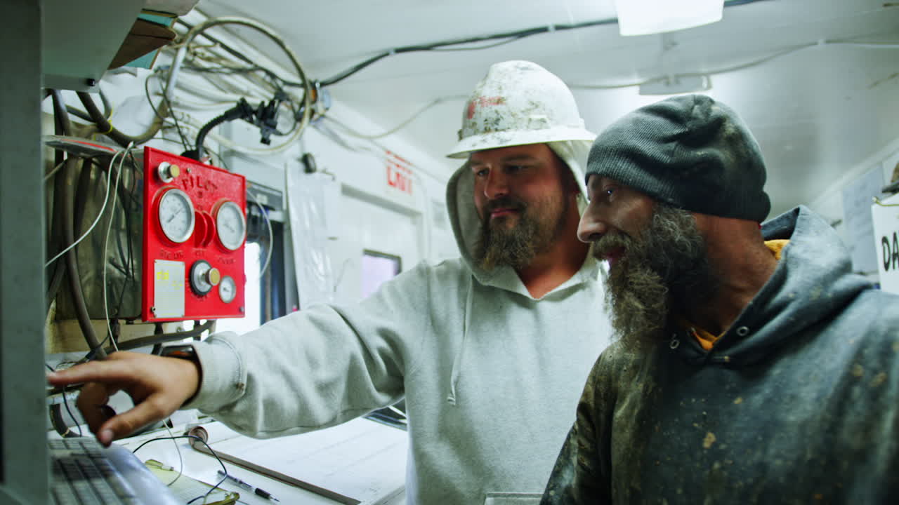 Two bearded men working in the site for oil production. Workers press the keys on the equipment operating the industry.
