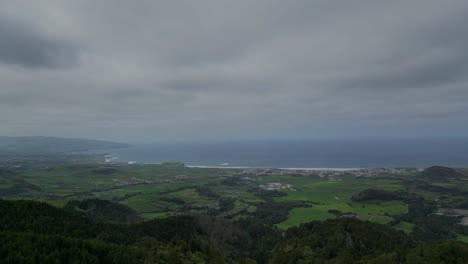 expansive view of a cloudy coastal landscape in the azores, portugal. rolling green fields meet the blue ocean under a dramatic overcast sky, blending natural beauty with atmospheric tranquility.