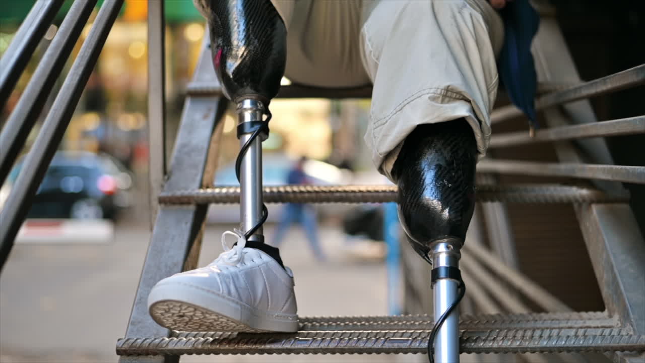 Slow motion view of a man with prosthetic legs and white sneakers sitting on a metal staircase