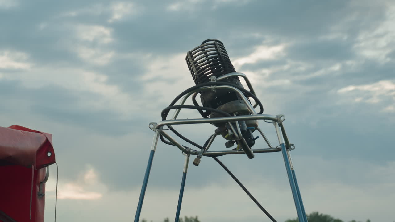 close up of twin burner assembly shaking on metal frame with blue support poles under cloudy sky, focus on dynamic movement and coil detail emphasising mechanical readiness for hot air balloon flight