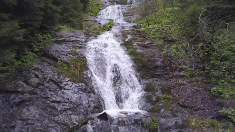 Ascending-aerial-view-of-Rausor-waterfall-from-drone-moves-from-low-close-up-to-wide-shot-of-cascades-through-forest