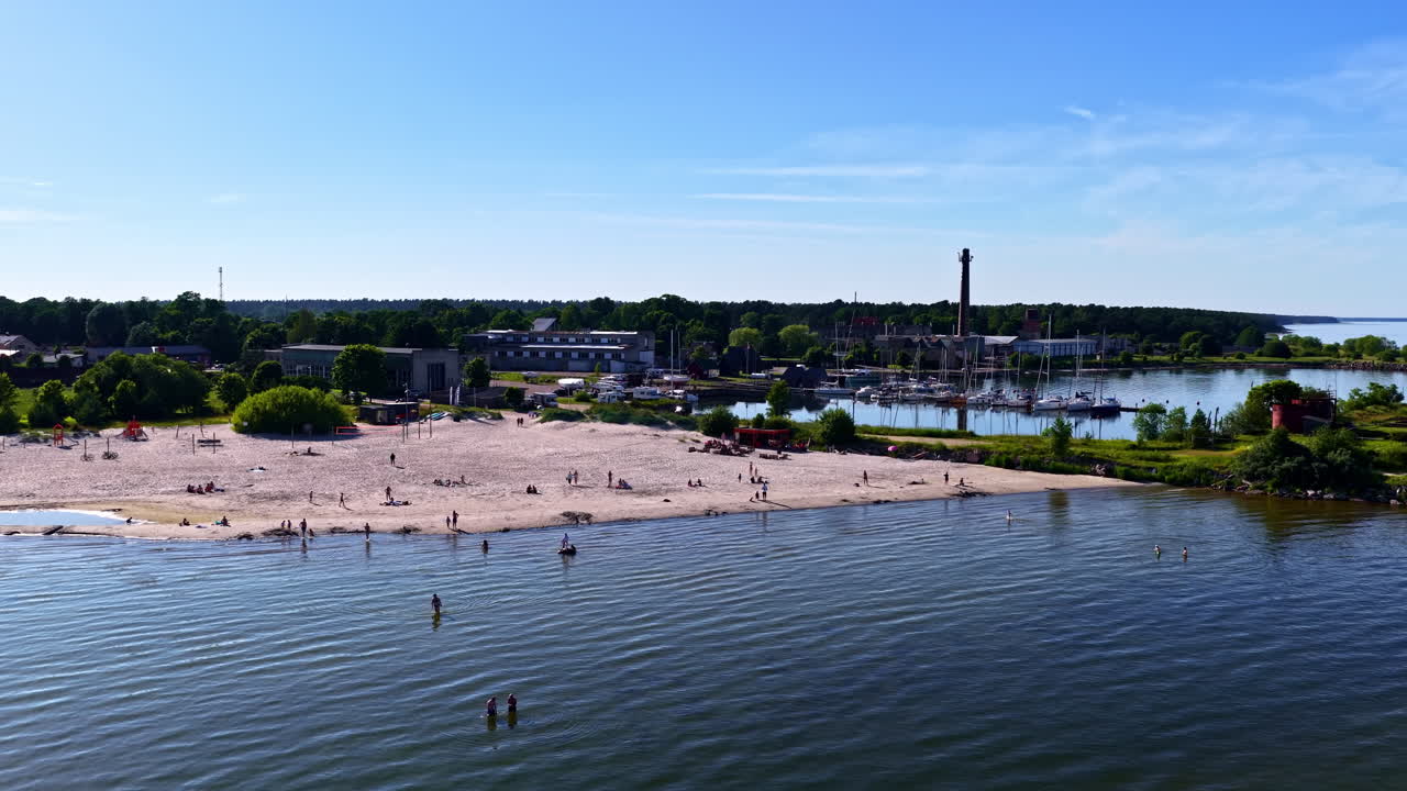 Aerial view of Engure beach in Latvia with people sunbathing and swimming, seen beside the harbor on a bright summer day