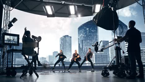 music clip studio set: shooting hip hop video dance scene with three professionals dancers performing on stage with big led screen with modern city background. director and cameraman in backstage.