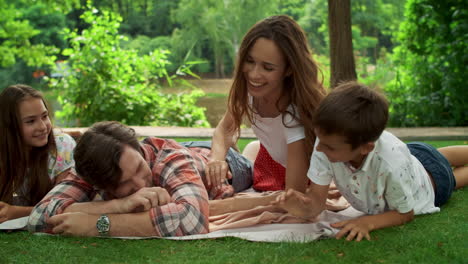 family lying on blanket in park. siblings with parents having fun in forest