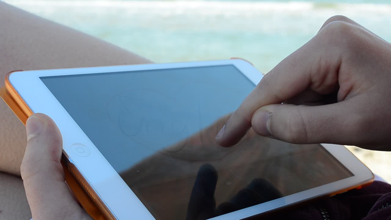 The tablet in the girl's hands on the beach. Work on the tablet. Shooting on the beach