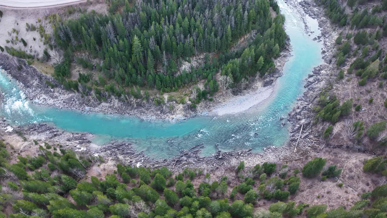 Aerial footage shows a turquoise river curving through dense evergreen forest and rocky terrain in Montana's Rocky Mountains near Glacier National Park