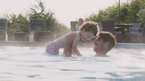 familia con hijo y hija bebé divirtiéndose en las vacaciones de verano salpicando en la piscina al aire libre