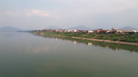 aerial view of the mekong river with reflection of chiang khan district houses on the water, drone flying forward on a foggy morning in thailand