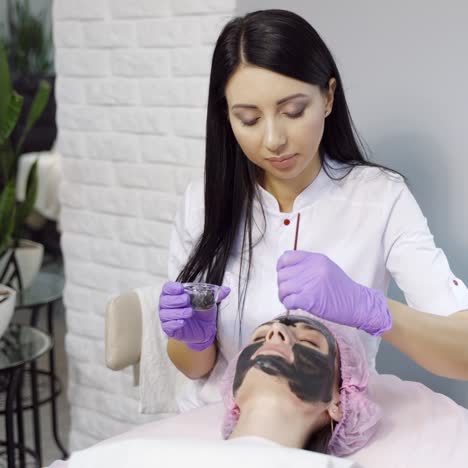 pretty cosmetologist with long hair makes a mask to a woman for cleansing the pores on the face in cosmetology. cosmetic procedures. spa