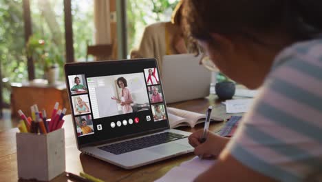 Girl-doing-homework-and-having-a-video-conference-with-teacher-and-classmates-on-laptop-at-home