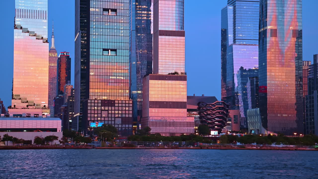 Horizonte da cidade de Nova York com o Vessel e o Empire State Building. Vista à beira-mar de modernas torres de vidro em Hudson Yards ao crepúsculo com reflexos rosados do pôr do sol.