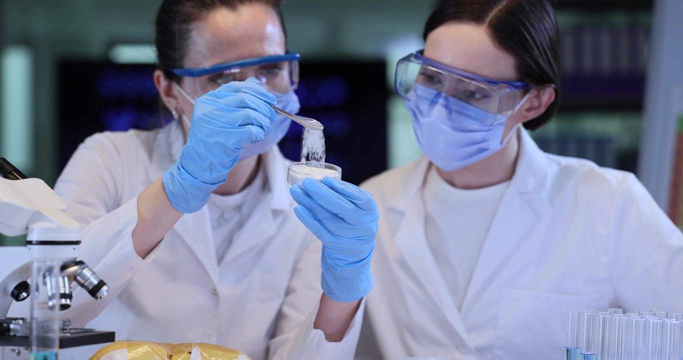 Female chemists in masks check white powder in flask in lab