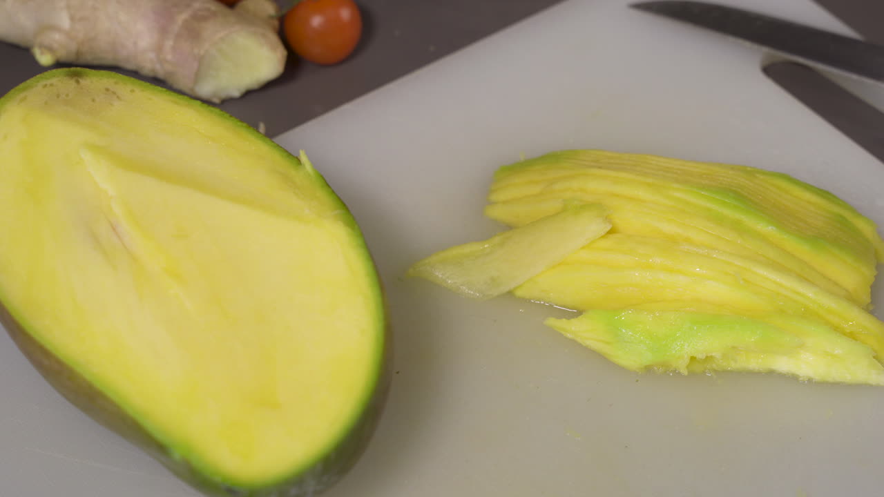Slicing A Ripe Green Mango On The Chopping Board With A Knife - closeup shot