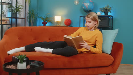 teenager boy reading book enthusiastically flipping pages thoughtfully looking up lying on sofa