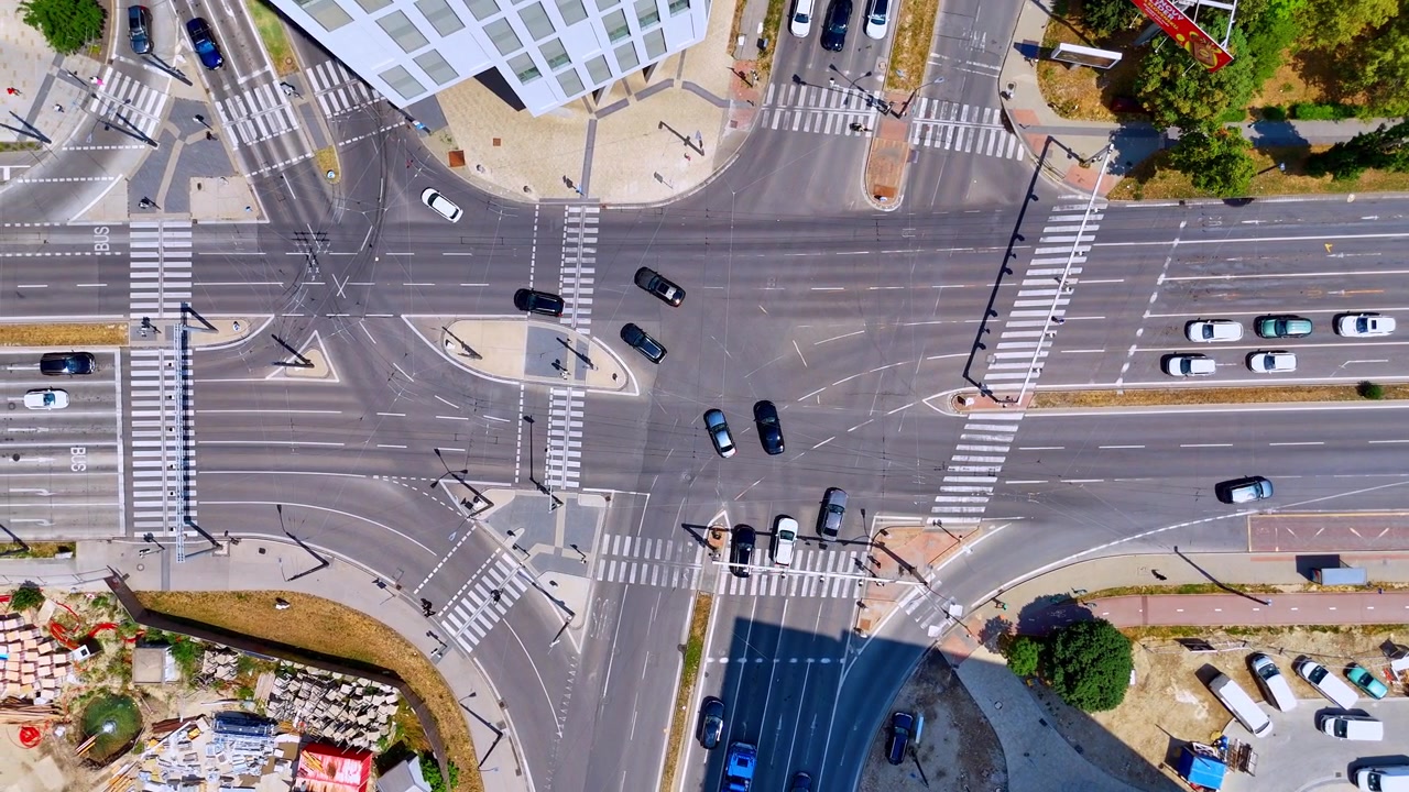Overhead view of a city street intersection, Bratislava, Slovakia. Drone perspective of white pedestrian crosswalks on dark asphalt road with moving cars during bright sunny day.