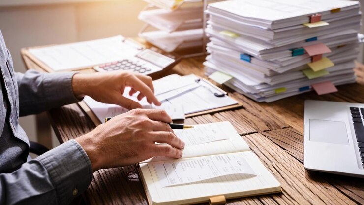 Sorting receipts, accountant in grey shirt comparing amounts with pen at desk by window, copy space