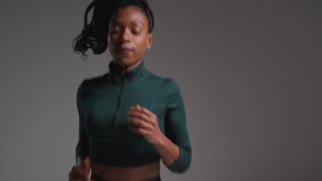 close up shot of female athlete wearing tracksuit training in gym fitness class running on the spot against plain background