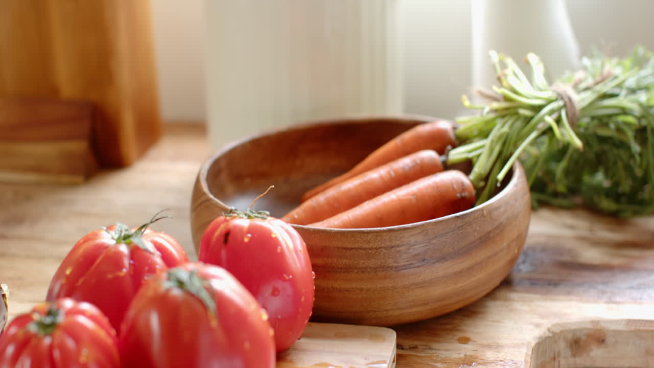 Fresh carrots in wooden bowl on kitchen counter with tomatoes nearby, at home