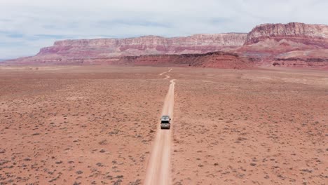 camper van on a road trip driving on single desert dirt road in utah, aerial