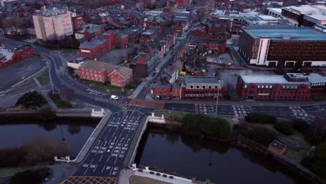 aerial view looking down city centre canal roundabout infrastructure suburban streets traffic at daybreak fast left orbit