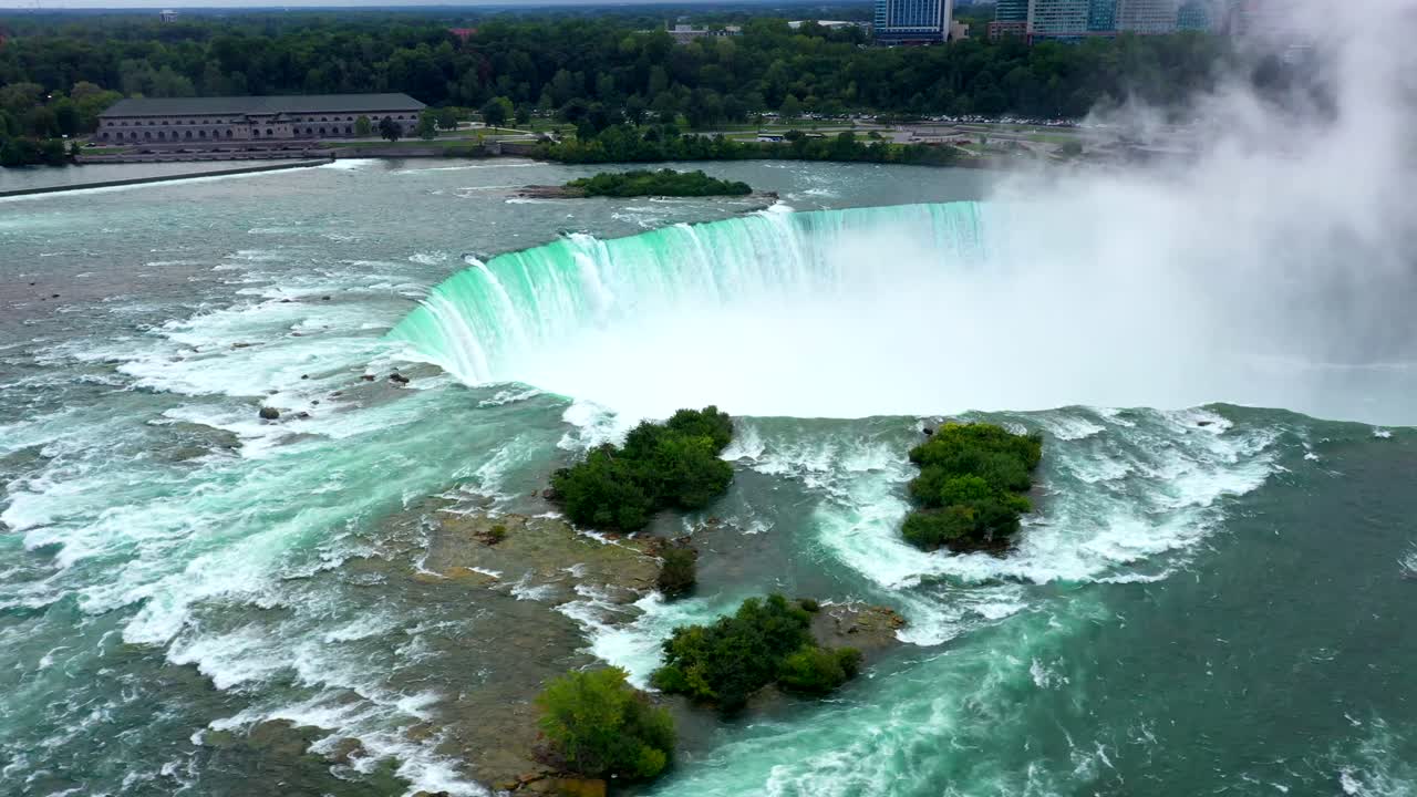 High drone orbit establishing of Niagara Falls showing massive curved drop and white mist rising upward