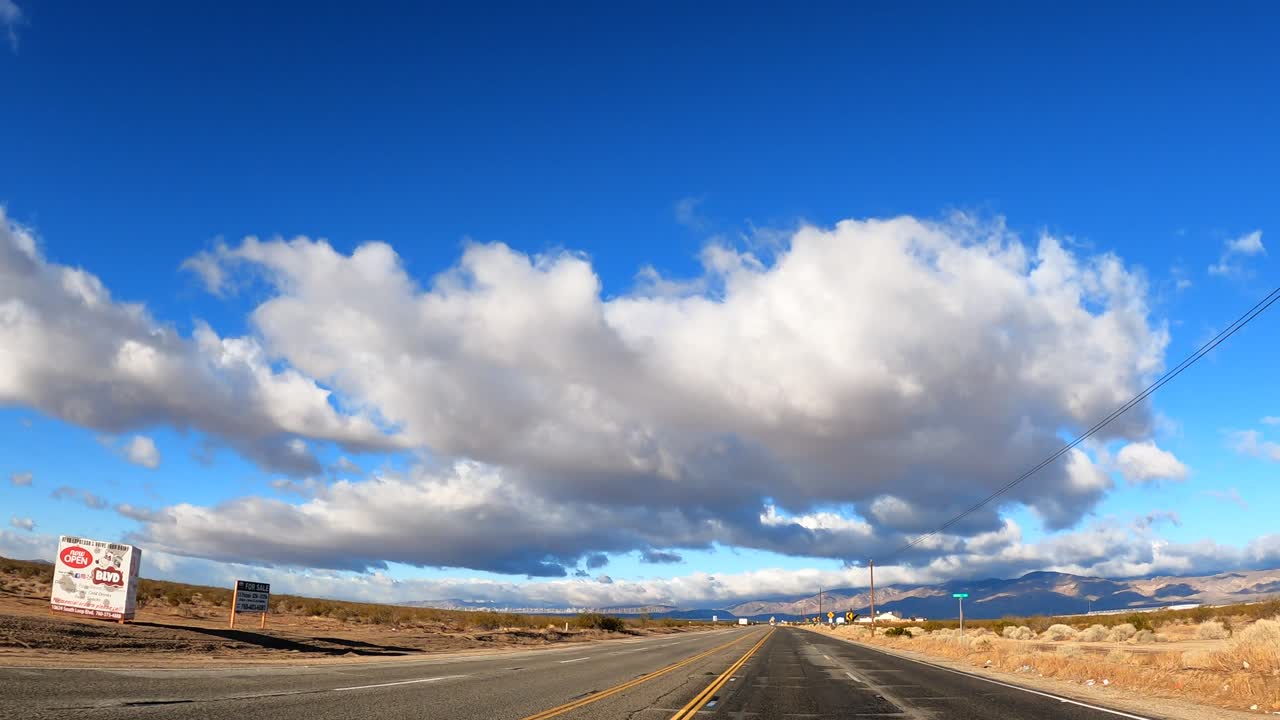 conduciendo a través del desierto de mojave con grandes formaciones de nubes en lo alto y las escarpadas montañas en la distancia - punto de vista
