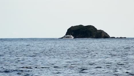 boat sailing in front of a small rocky island on the south pacific ocean