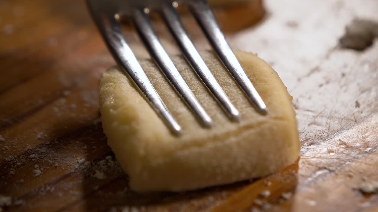 4K close up shot pressing fresh raw homemade gnocchi  with a silver fork on a wooden table
