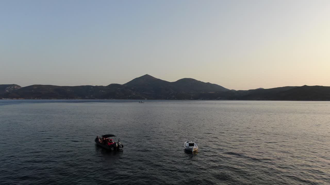 vista de avión no tripulado en grecia volando sobre el mar azul con barcos montañas en el horizonte en milos al atardecer