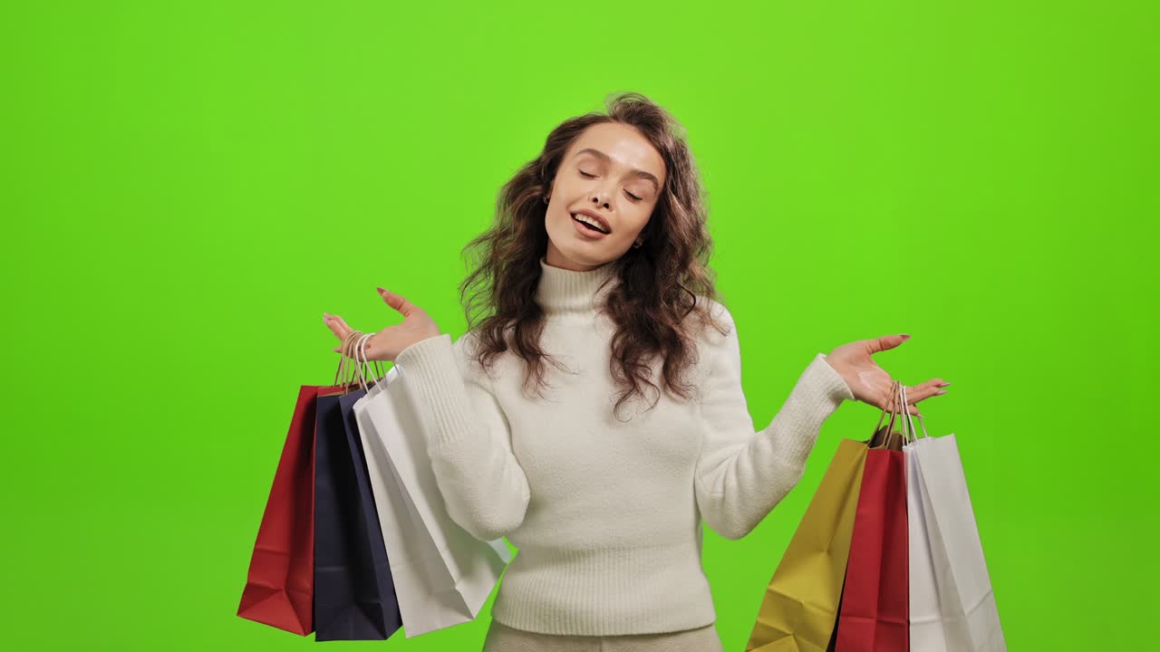 여성은 카메라를 보고 미소 짓고 쇼핑 가방을 흔들며 초록색 바탕에 서 있습니다.