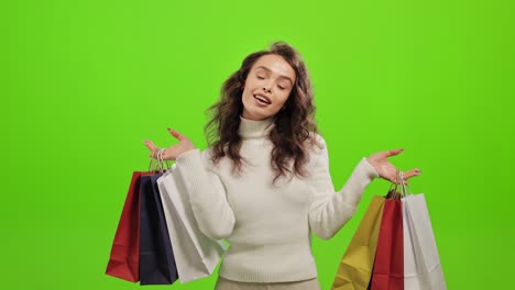 la mujer está mirando a la cámara y sonriendo. está agitando las bolsas de compras. está de pie sobre un fondo verde. pantalla verde. 4k.