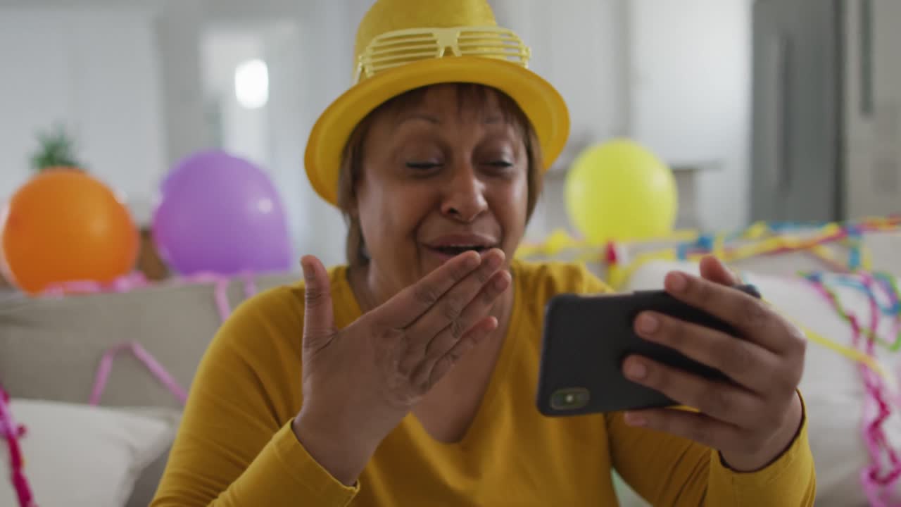 Happy african american senior woman making new year's eve smartphone video call blowing kisses