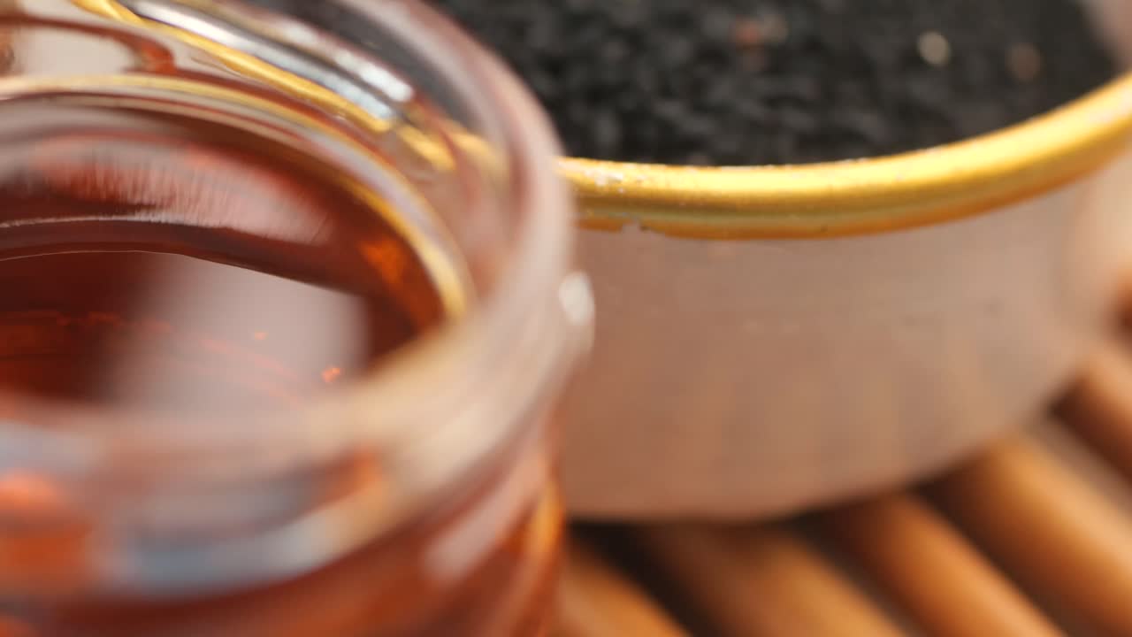 Close-up of amber liquid in a jar with black seeds in the background