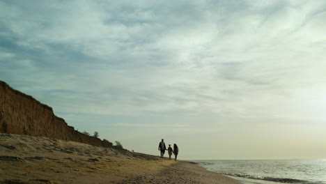 siluetas familiares caminando por la orilla de arena junto a la playa. concepto de relajación vacacional.