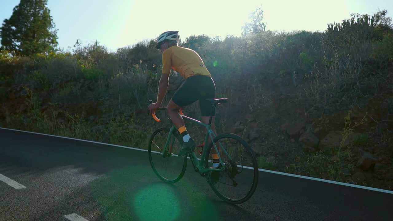 Against the serene backdrop of the morning, a man cycles on a road bike for outdoor exercise along an unoccupied road. The slow-motion perspective intensifies the thrill of extreme sports