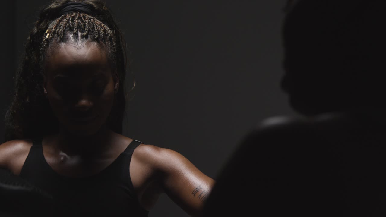 foto de estudio de una mujer poniéndose guantes de boxeo lista para pelear con un entrenador