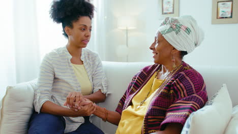 young black woman holding hands and talking with senior mother at home